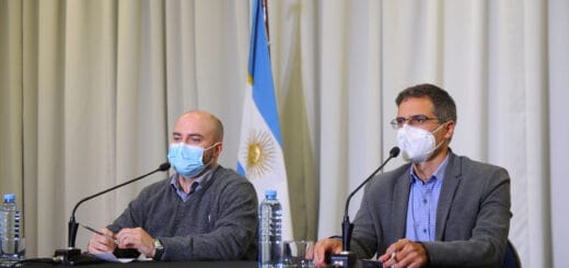 alt="en la fotografía puede verse a dos personas sentadas en una mesa, frente a dos micrófonos; detrás una bandera argentina y un cortinado"