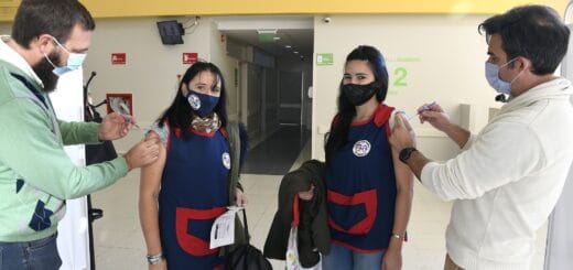 alt="en la fotografía, dos docentes de sexo femenino son vacunadas por dos personas de sexo masculino"