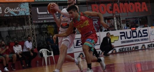 alt="en la fotografía puede verse a dos basquetbolistas corriendo, uno lleva una pelota en sus manos y a su costado va un rival; detrás se observa un hombre en cuclillas, fuera del campo de juego.