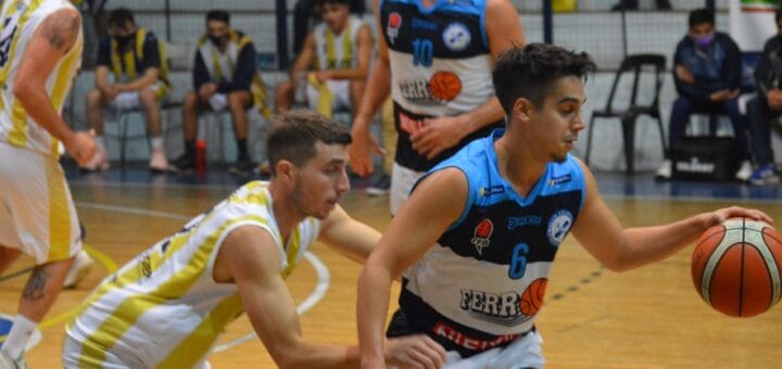 alt="en primer plano se puede ver a un jugador de básquet picando la pelota y a otro que quiere quitársela; atrás dos jugadores observan, al fondo los bancos de suplentes"