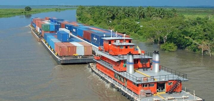 alt="un remolcador impulsa barcazas por un cauce fluvial"