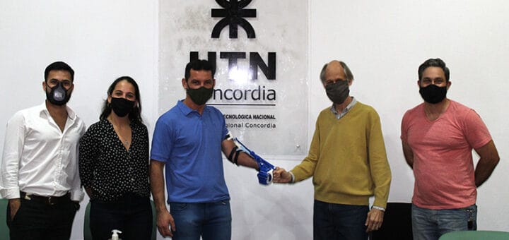 alt="en la imagen puede verse, a cinco personas, dos de ellas tienen detrás un cartel de la UTN Concordia"