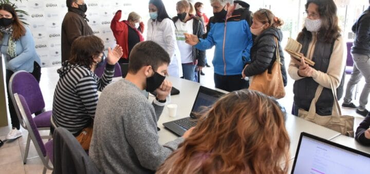 alt="en la fotografía puede verse a varias personas registrándose para recibir la vacuna contra el coronavirus, las atienden voluntarios que los inscriben en computadoras"