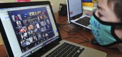 alt="en la imagen puede verse, en primer plano, un niño frente a una pantalla de computadora, más atrás se ve otra pantalla de computadora"