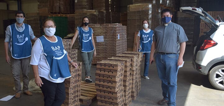 alt="en la fotografía, cuatro mujeres y un hombre junto a mercaderías del banco de alimentos, en la izquierda se ve un automóvil con el baúl abierto"