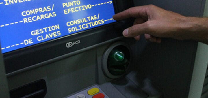 alt="en la imagen parte de una mano y parte de una pantalla de un cajero automático"