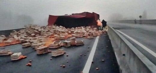 alt="en primer plano, cajones de citrus desparramados en una ruta, al fondo un camión atravesado en el camino"