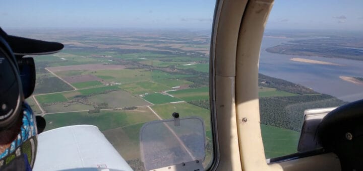 alt="en la imagen se ve una vista aérea desde la cabina de un avión, también aparece parte del rostro del piloto"