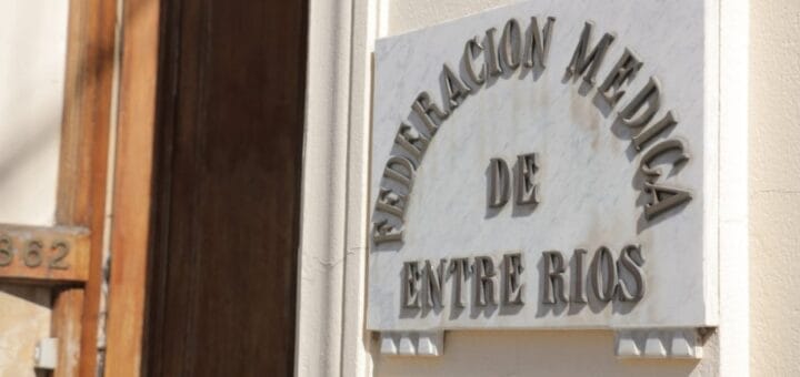 alt="en la imagen puede verse una placa adosada a la pared con la inscripción: Federación Médica de Entre Ríos, al lado hay una puerta abierta"