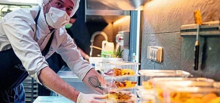 alt="en la imagen puede verse a un trabajador gastronómico, con barbijo, preparando comida para llevar en recipientes herméticos"