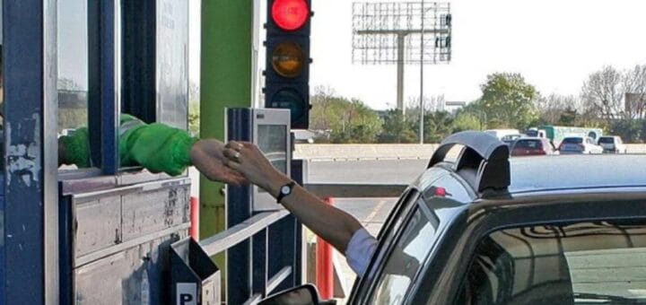 alt="en la imagen se puede ver una cabina de peaje de la que sale una mano que se encuentra con otra que sale de la ventanilla de un auto"