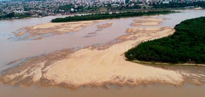 alt="en la imagen puede verse un río con bancos de arenas, dos islas y una ciudad en el fondo"