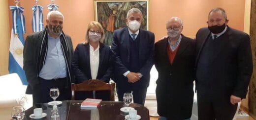 alt="en la imagen, cuatro personas paradas, con barbijos, en la punta de una mesa que está en primer plano"