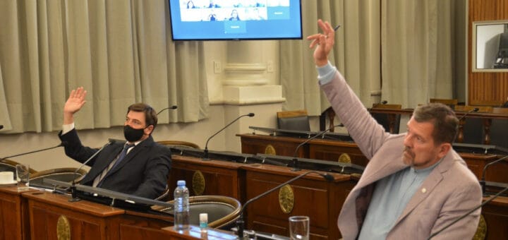 alt="en la imagen dos senadores levantan la mano para votar en el recinto del senado de entre ríos"
