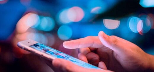 alt="en la imagen puede verse una mano que sostiene un teléfono celular y otra que se encuentra sobre la pantalla"