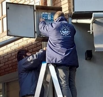 alt="dos trabajadores municipales trabajan en el controlador de un semáforo"