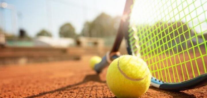 alt="en la imagen, una pelota de tenis, al lado de una raqueta, al fondo otra pelota de tenis"