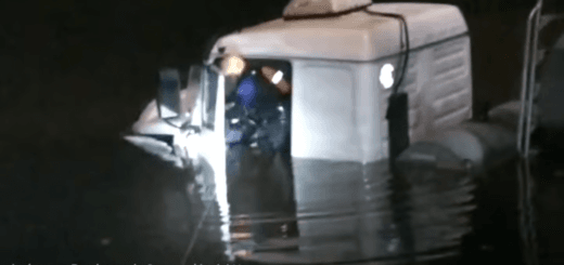 alt="en la imagen puede observarse a un bombero rescatando a un camionero de la cabina del camión que cayó en un curso de agua"