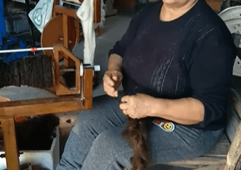 alt="en la imagen puede verse a una artesana hilando lana cruda"