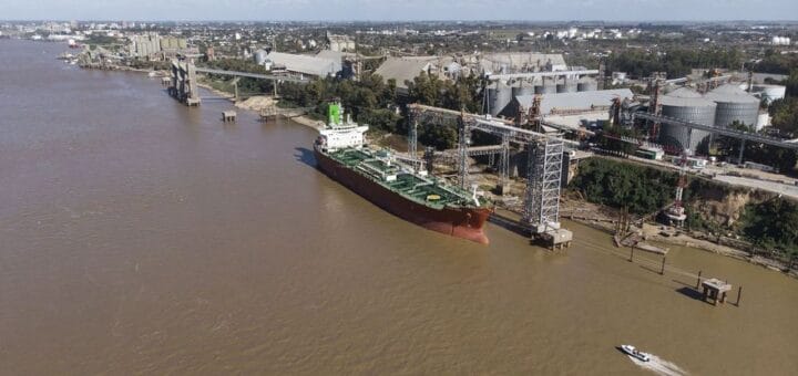 alt="en la imagen puede verse un puerto fluvial con barcos cargando cereal y algunas lanchas navegando"
