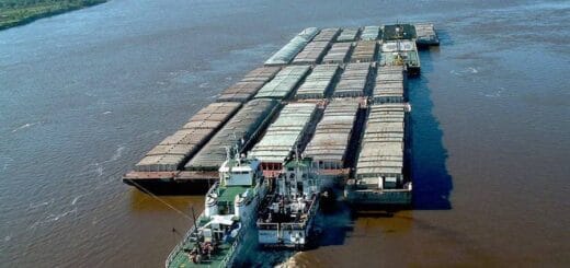 alt="en la imagen, dos remolcadores empujan un tren de barcazas por un río"