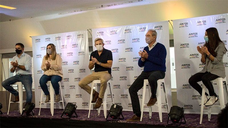 aalt="en la imagen puede verse a tres hombres y dos mujeres sentados en bancos"