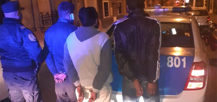 alt="en la imagen puede verse a tres personas detenidas y a dos policias, junto a un patrullero"