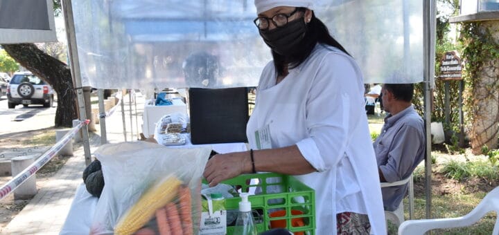 alt="en la fotografía puede verse a una mujer totalmente vestida de blanco y con un barbijo negro preparando comestibles para vender"