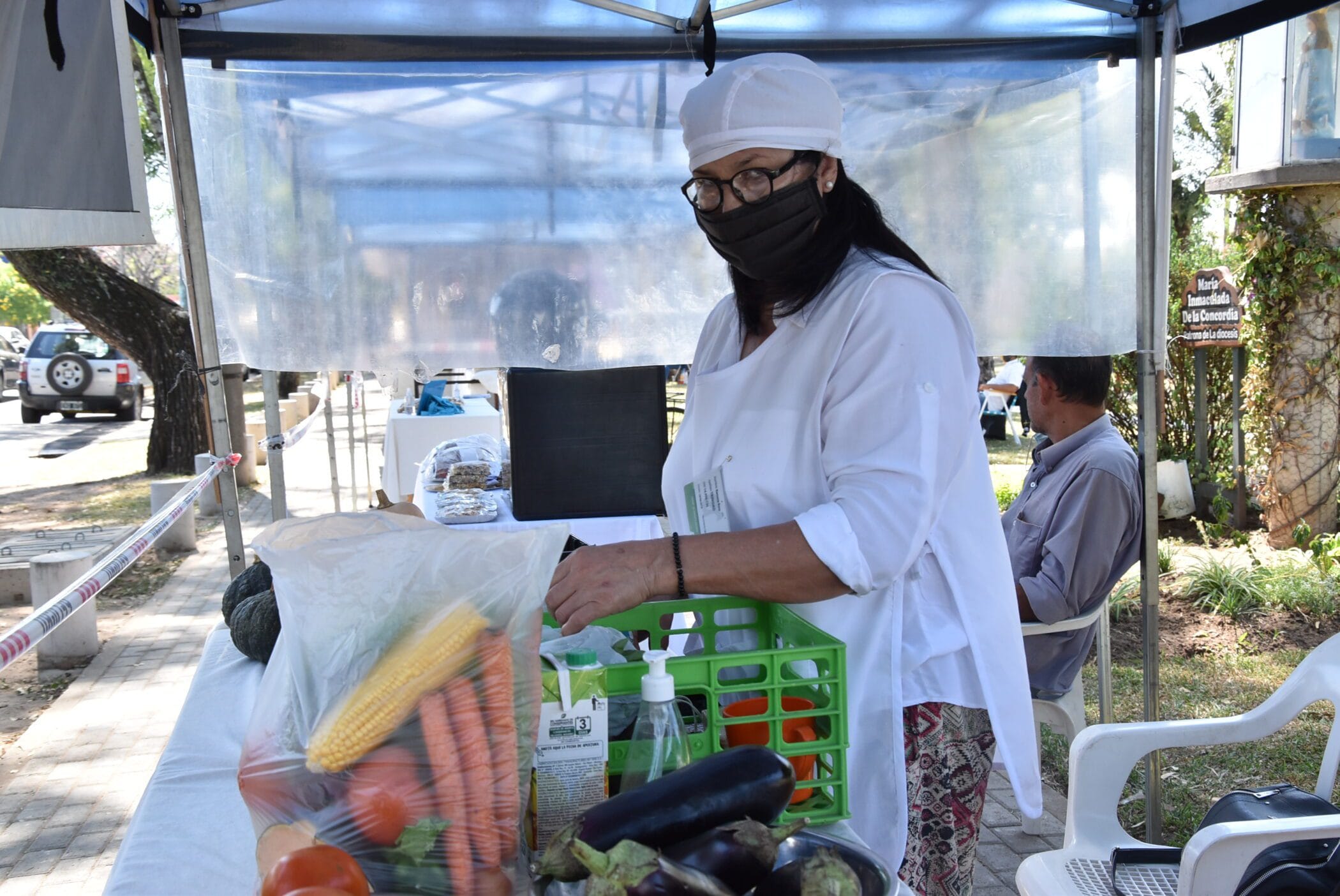 alt="en la fotografía puede verse a una mujer totalmente vestida de blanco y con un barbijo negro preparando comestibles para vender"