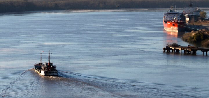 alt="un barco navegando en un río y otro amarrado en un puerto"