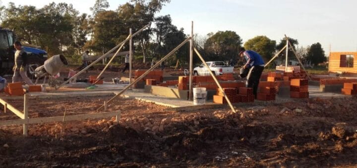 alt="en la imagen puede verse a varios hombres trabajando en la construcción de una vivienda"