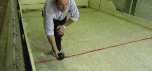 alt="en la imagen puede verse al ex intendente de Villa del Rosario, agachado, con un elemento redondo en la mano derecha, en una cancha de bochas"