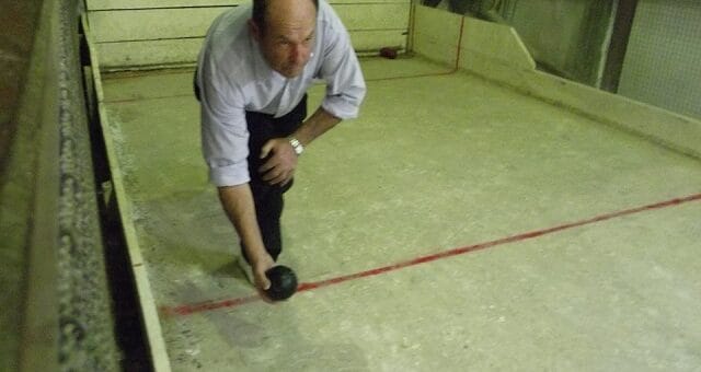 alt="en la imagen puede verse al ex intendente de Villa del Rosario, agachado, con un elemento redondo en la mano derecha, en una cancha de bochas"