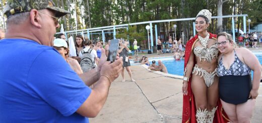 alt="un hombre le saca fotos a una joven reina del carnaval y a una mujer, detrás una piscina en la que hay varias personas"
