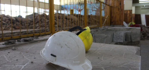 alt="en la imagen puede verse en primer plano dos cascos de obreros de la construcción sobre el piso, detrás una estructura de madera de una obra en construcción en una de las 605 escuelas entrerrianas"