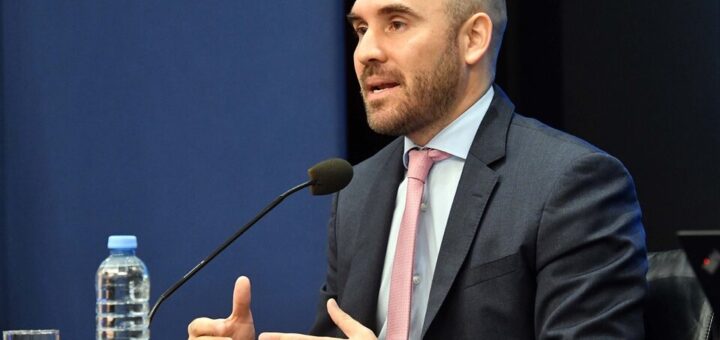 alt="en la imagen, el ministro de economía martín guzmán habla ante un micrófono ubicado en una mesa, en la izquierda, adelante del micrófono, hay una botella de agua"