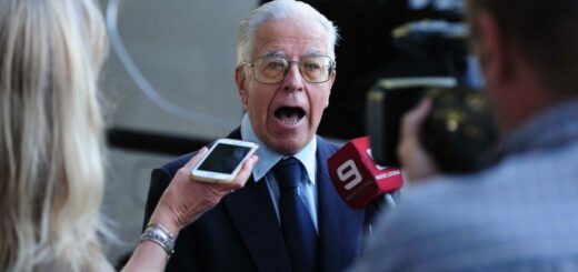 alt="un hombre de pelo blanco habla ante un micrófono y un teléfono celular"