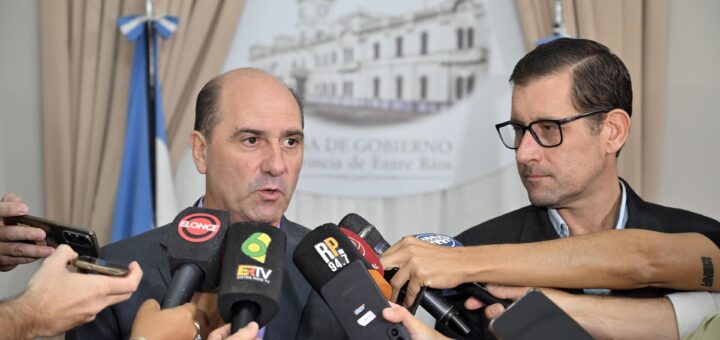 alt="un hombre realiza anuncios ante micrófonos y otro lo observa"