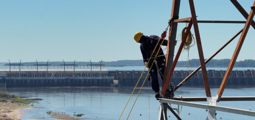 alt="Operarios instalando equipos sobre una torre metálica para la prueba de sirenas de Salto Grande con el río y la represa de fondo"