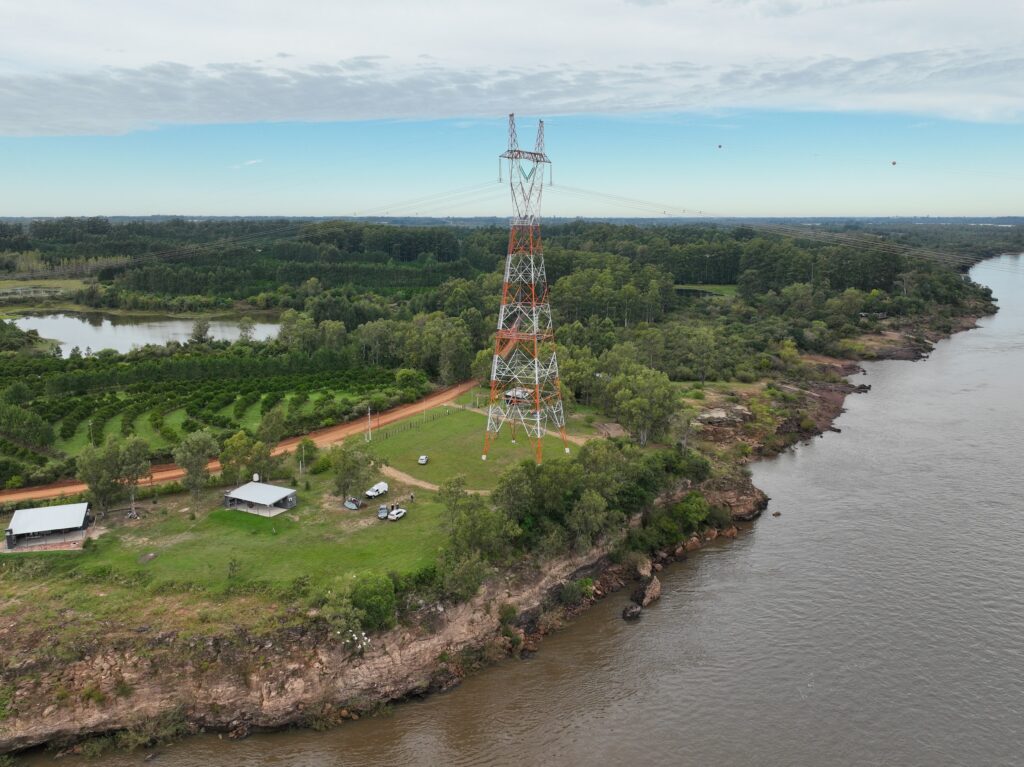 alt="Vista aérea de una torre de alta tensión junto al río Uruguay donde funciona el Sistema de Aviso Sonoro en Salto Grande"