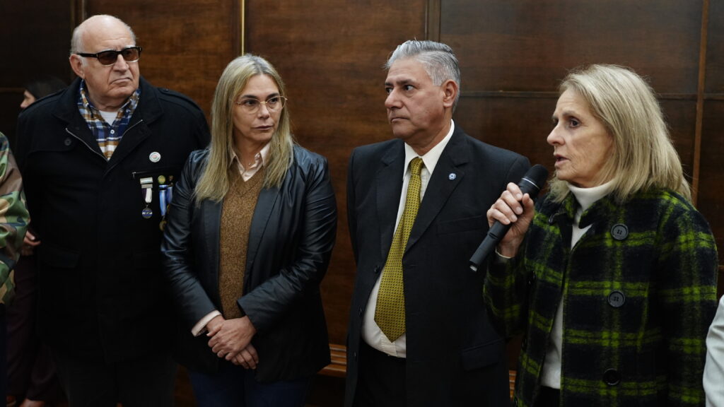 alt="La viceintendente Magdalena Reta de Urquiza sosteniendo un micrófono junto a Veteranos de Malvinas durante la sesión en que se realizó el tratamiento del procedimiento administrativo en Concordia"