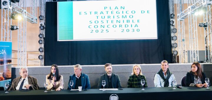 alt="Autoridades de Concordia y Entre Ríos sentadas en una mesa frente a una pantalla que anuncia el Plan Estratégico de Turismo sostenible en Concordia"