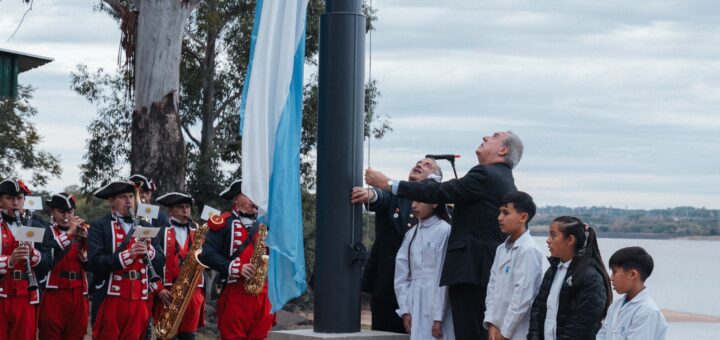 alt="Izamiento de la bandera nacional junto al lago en el acto del 25 de Mayo en Salto Grande con presencia de escolares y autoridades"
