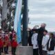 alt="Izamiento de la bandera nacional junto al lago en el acto del 25 de Mayo en Salto Grande con presencia de escolares y autoridades"