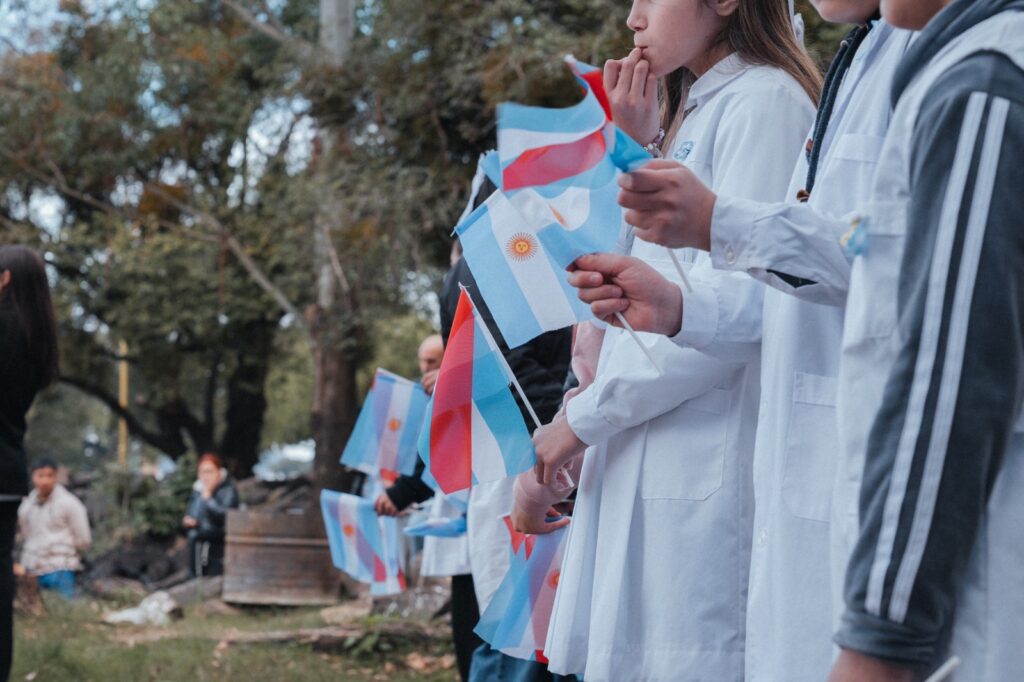 alt="Alumnos de escuelas entrerrianas sosteniendo banderas de mano celestes y blancas en el acto del 25 de Mayo en Salto Grande"