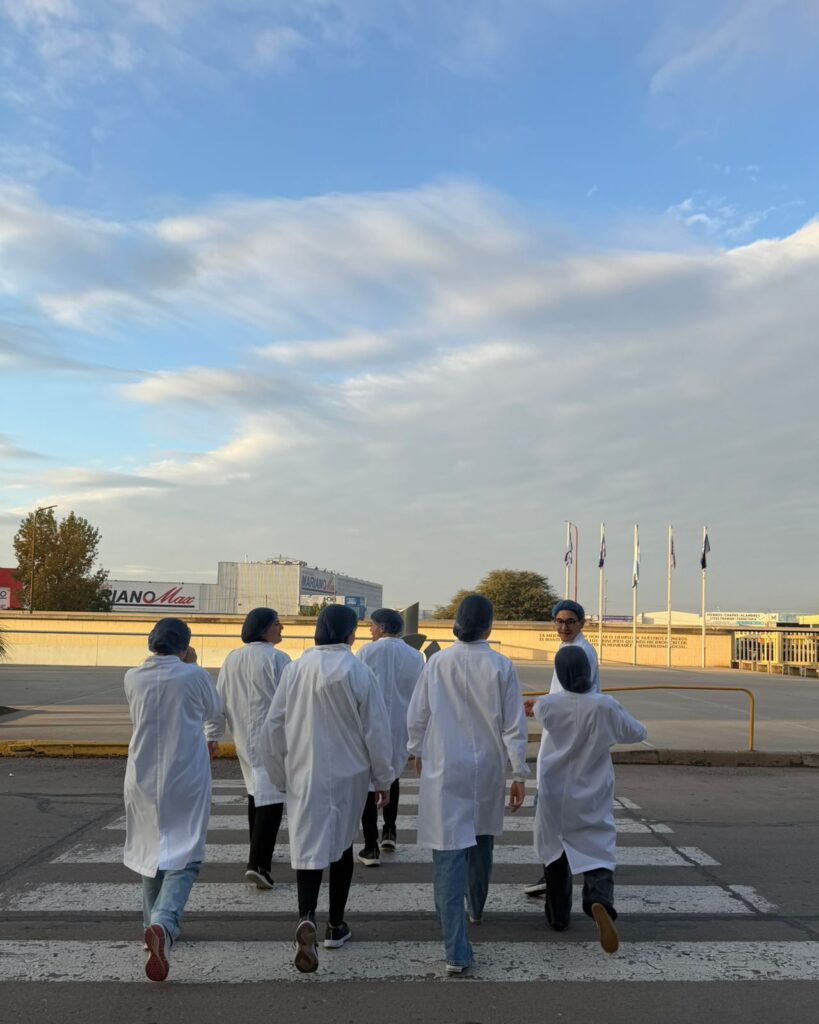 alt="Vista de espaldas de estudiantes de la carrera de Contador Público caminando con batas de laboratorio hacia el sector productivo."