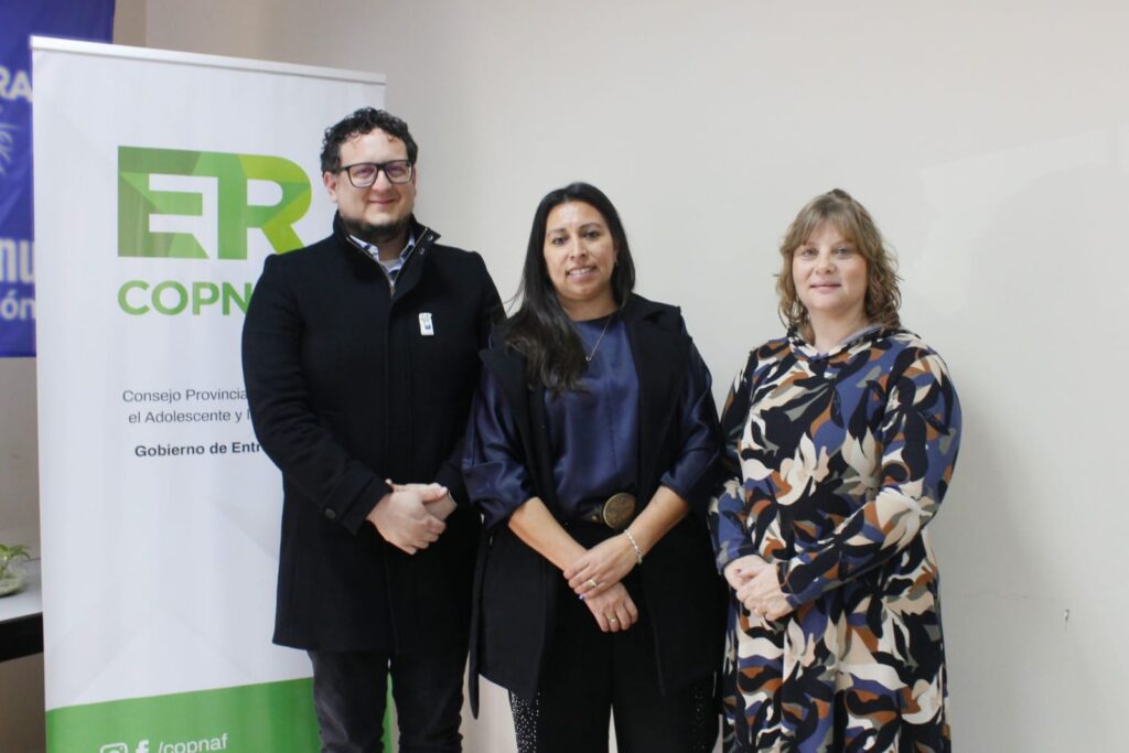 alt="Tres directivos del Copnaf posan ante un banner institucional en la jornada de capacitación técnica para los equipos de niñez en Concordia"