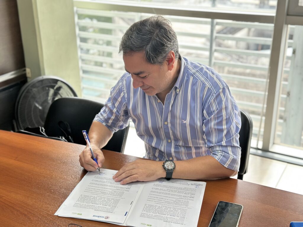 alt="Eduardo Cristina, titular de Codesal, de camisa celeste y blanca a rayas, firmando las hojas del convenio entre Codesal y la Dirección General de Estadística y Censos"