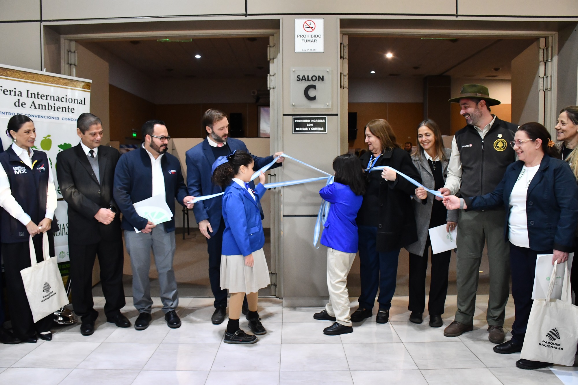 alt="Estudiantes de primaria cortan una cinta celeste y blanca acompañados por funcionarios en la inauguración de la Feria Eco Ciencias."