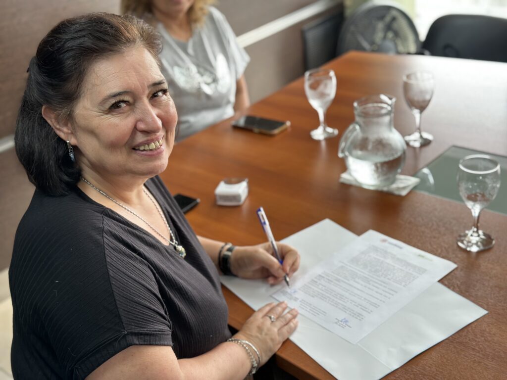 alt="Andrea Cottonaro, directora de Estadística y Censos de Entre Ríos, firma los papeles del convenio entre Codesal y la Dirección General de Estadística y Censos sobre una mesa marrón"
